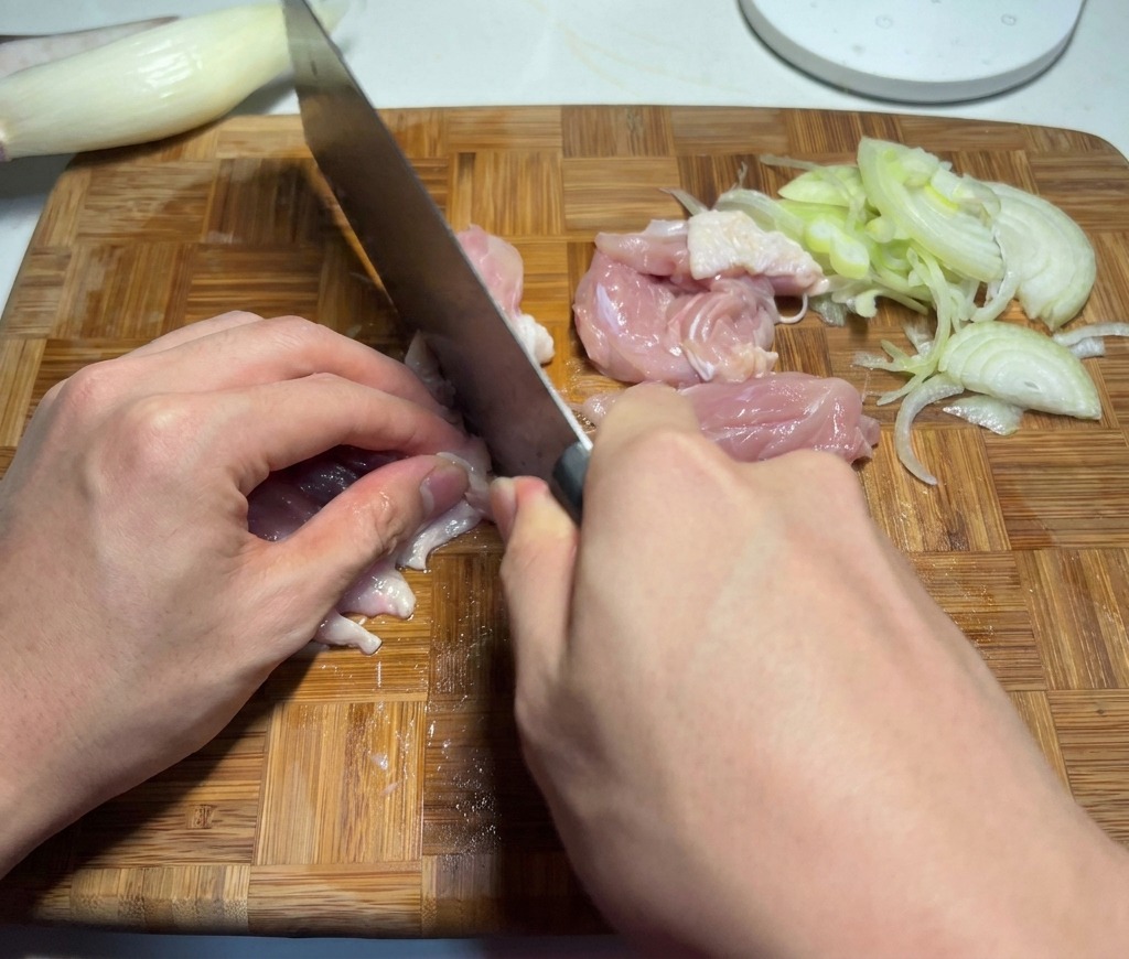まな板の上で、生の鶏もも肉を一口大のサイズに切り分けているシェフの手元。