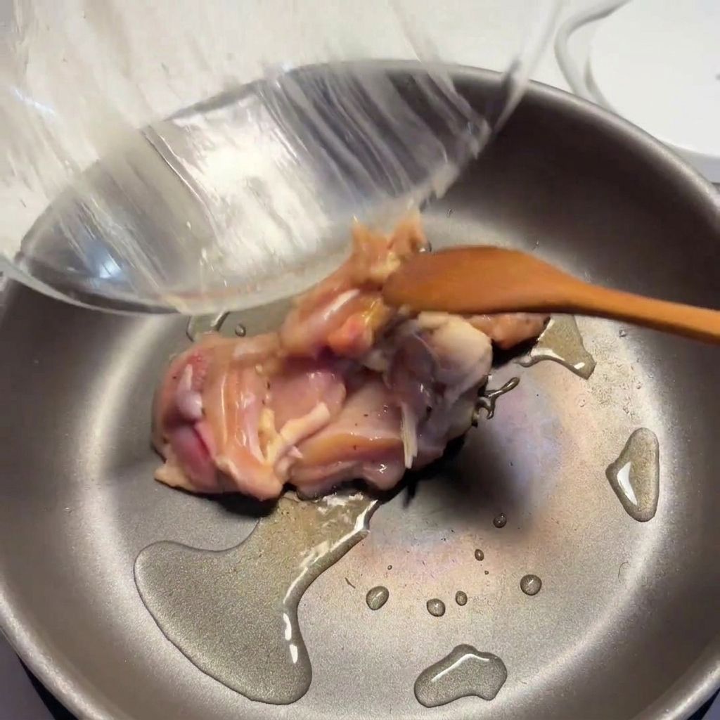 熱したフライパンで、油を引いて下味をつけた鶏肉の表面をこんがりと焼いている様子。