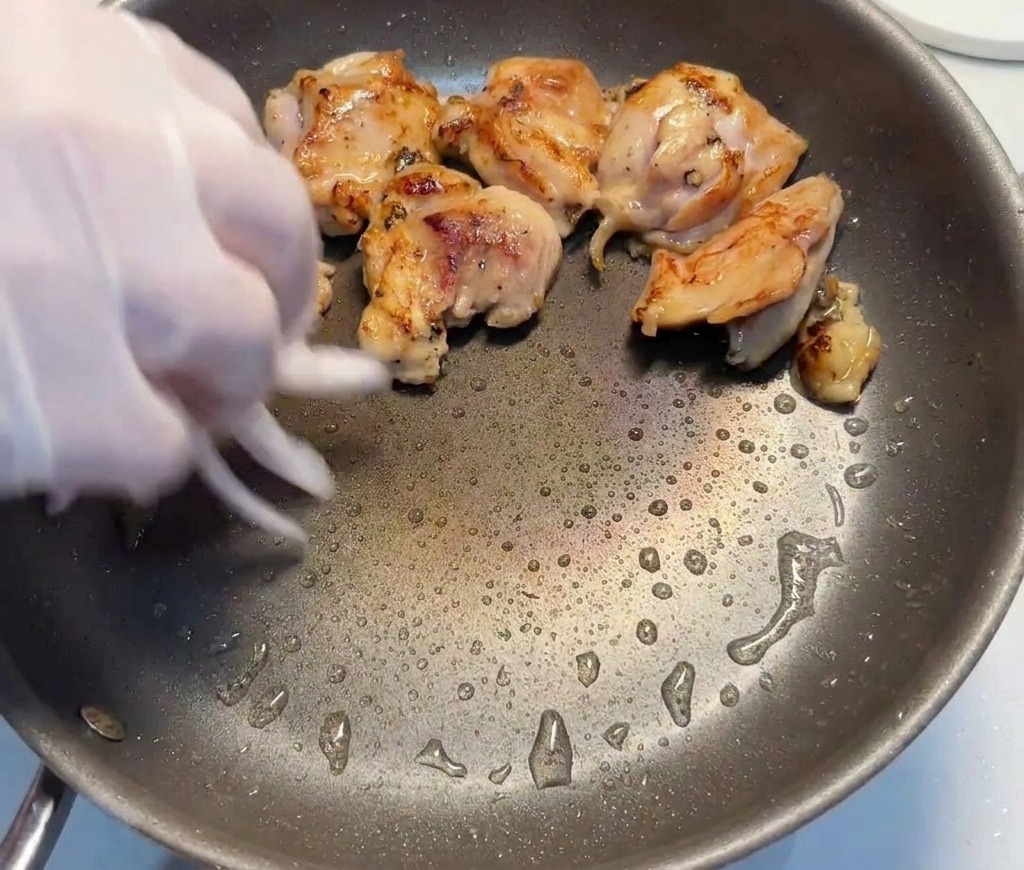 鶏肉が焼けているフライパンに、スライスした赤玉ねぎをたっぷり投入している様子。