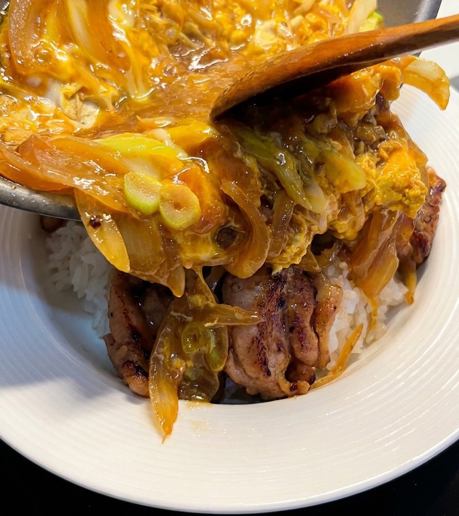 ご飯と鶏肉が入ったボウルに、フライパンからとろとろの卵と玉ねぎを滑らせるように盛り付けている様子。