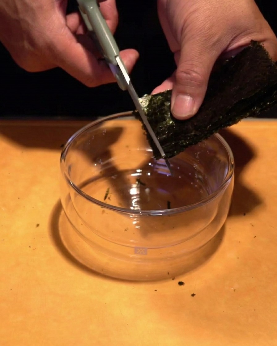 ボウルの上で、キッチンバサミを使って焼き海苔を細い千切りにしている様子。