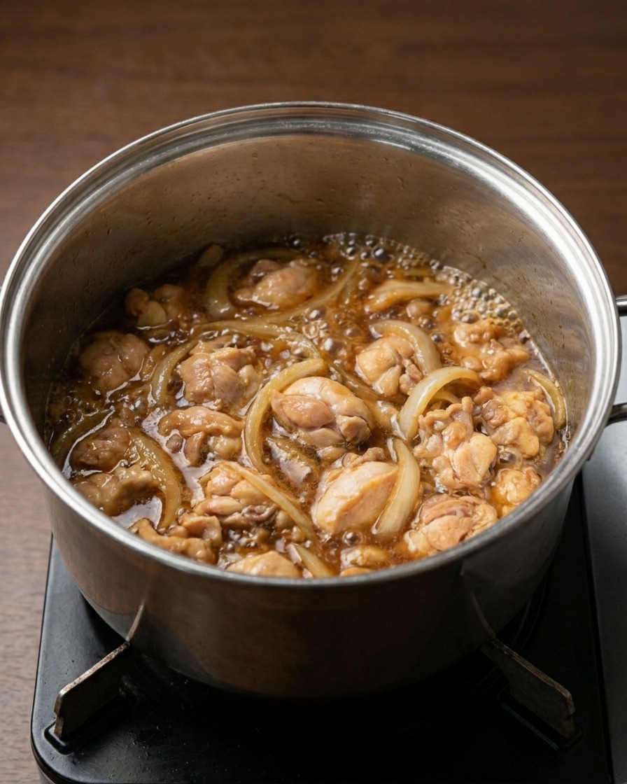 濃い茶色の煮汁の中で、鶏肉と玉ねぎがグツグツと煮えている様子。