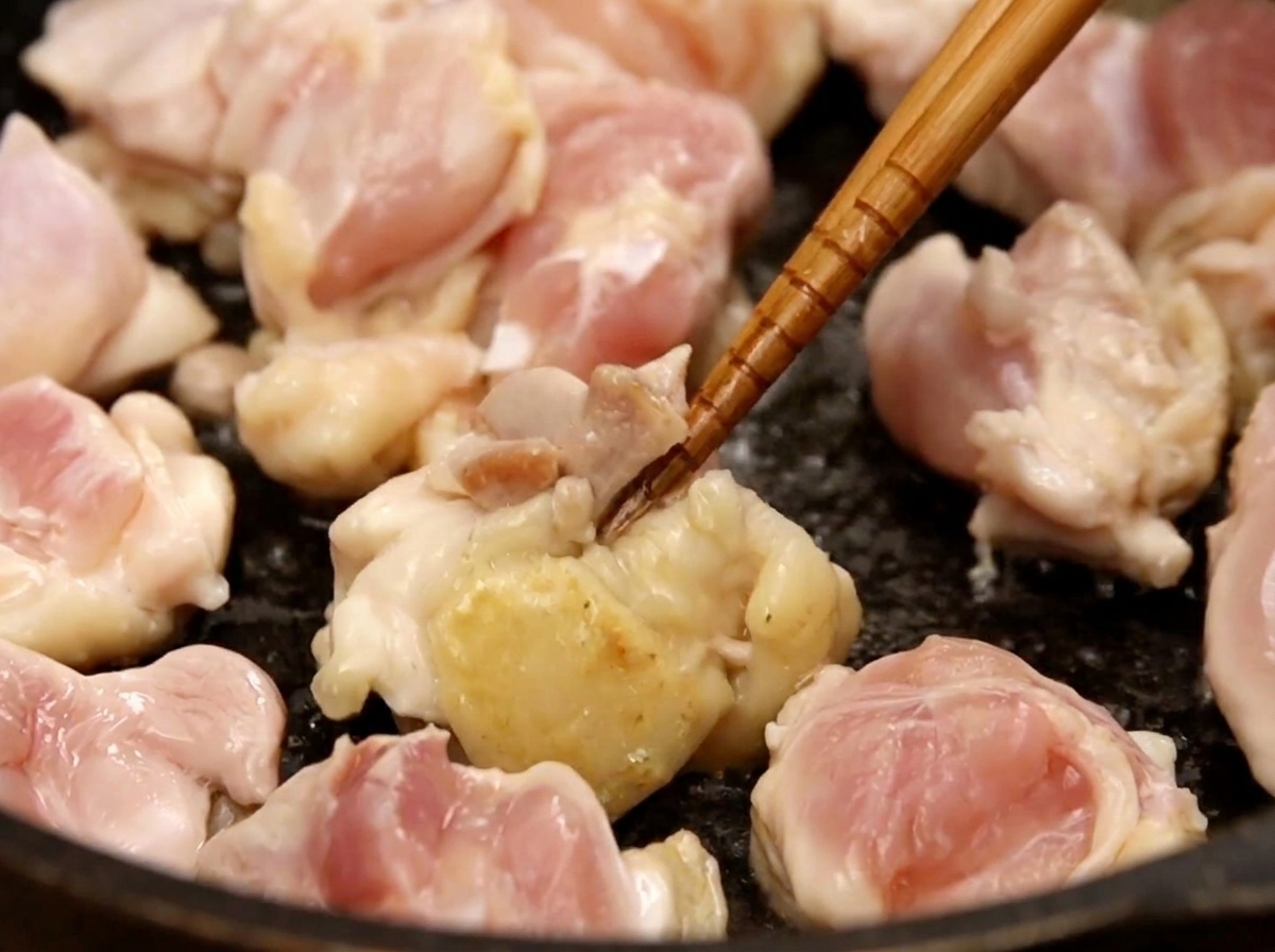 フライパンで一口大の鶏肉を菜箸で炒め、表面に軽く焼き色がついてきた様子。