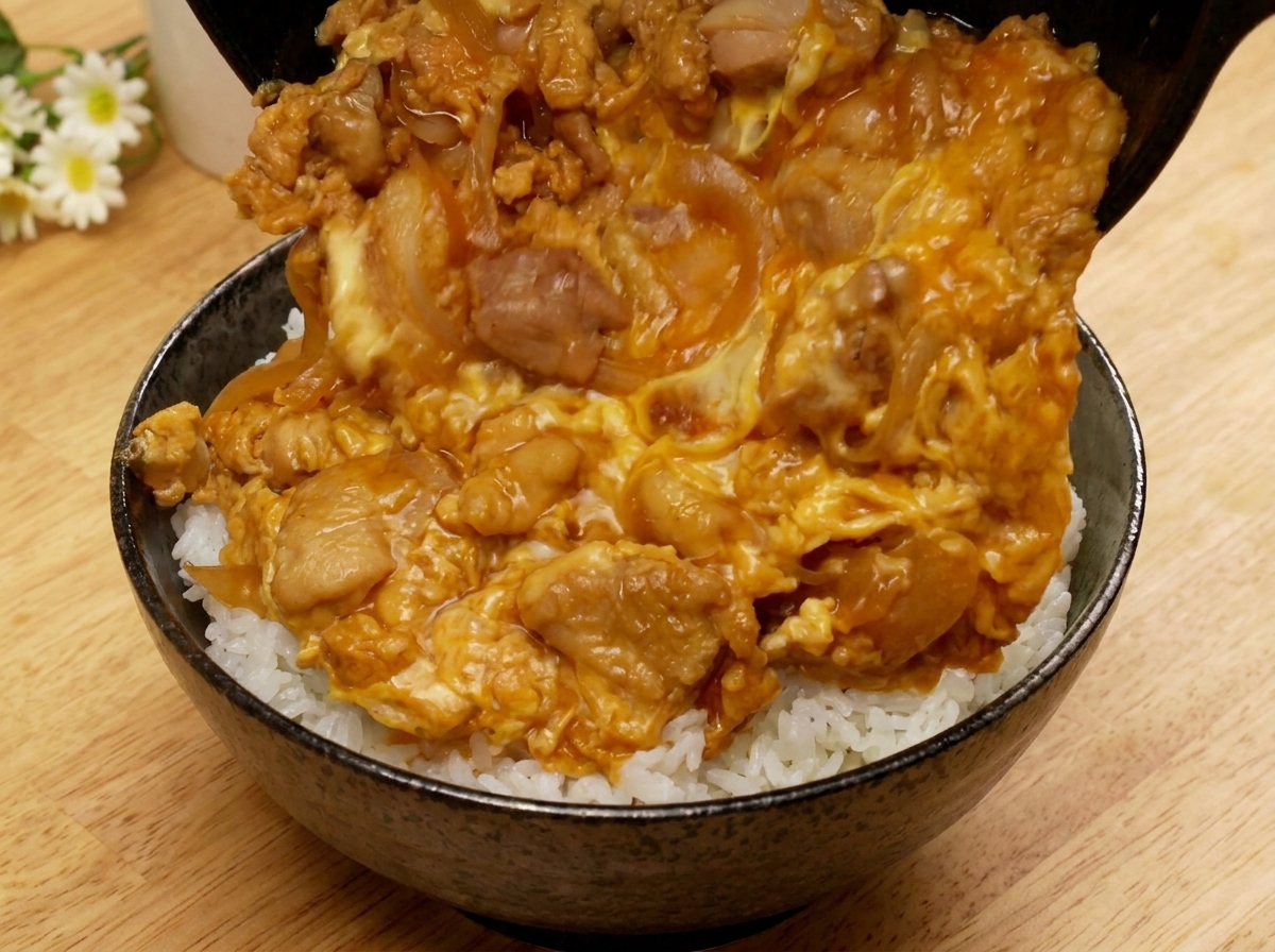 フライパンを傾け、出来上がった親子丼の具をご飯の入った丼へ滑らせるように移している様子。