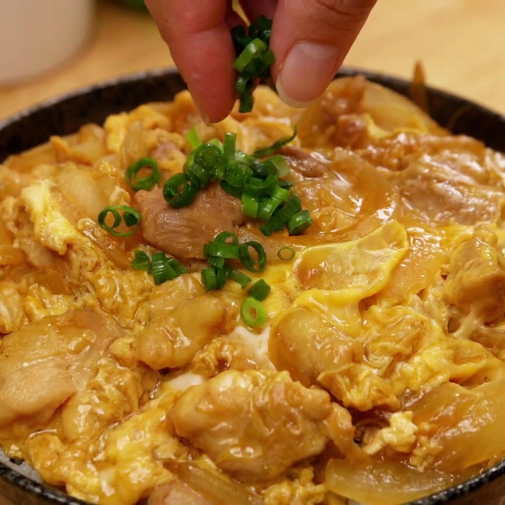 完成した親子丼の真ん中に、刻んだねぎをふんわりとトッピングしている様子。