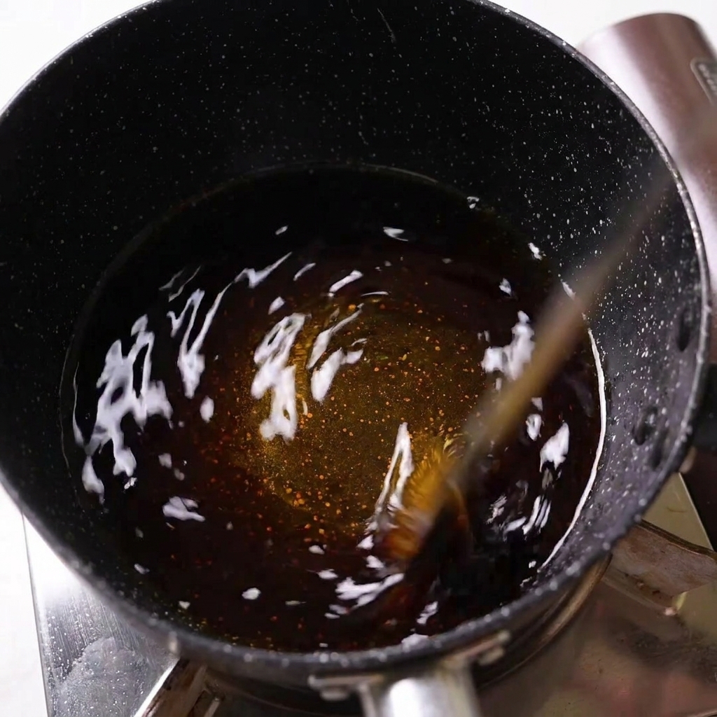 コンロの上の黒い鍋で、濃い色の調味料が煮立っている様子