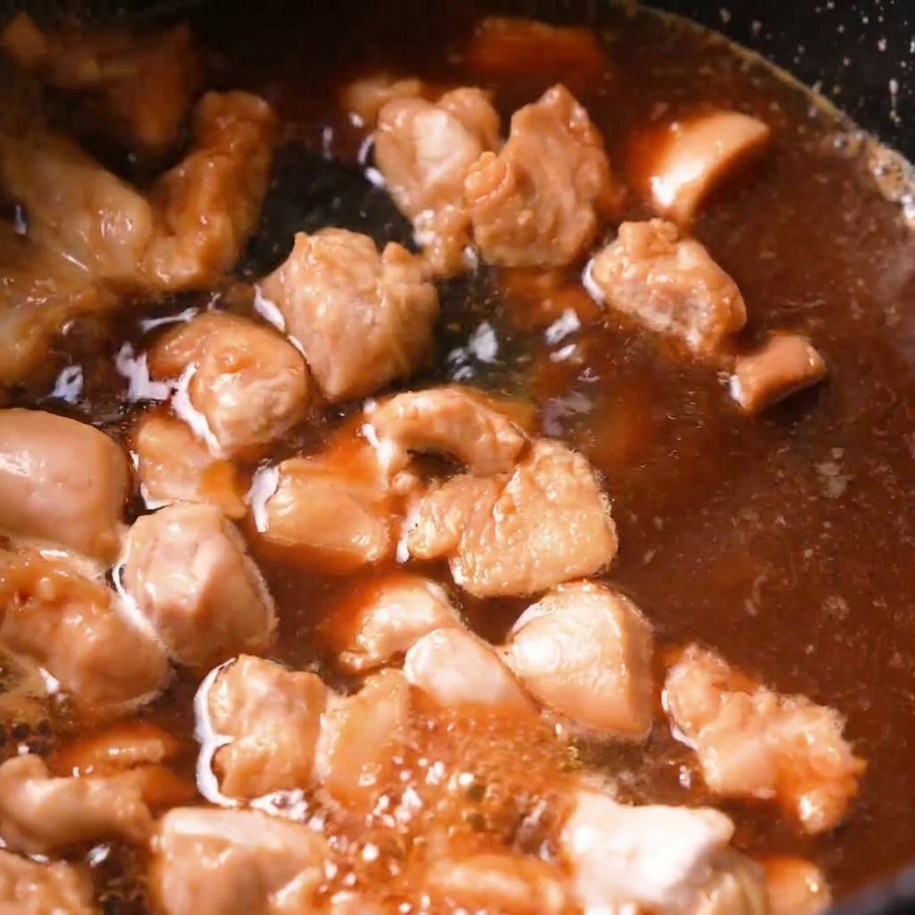 黒い鍋の中で、鶏肉が茶色いだし汁と一緒にグツグツと煮込まれている様子