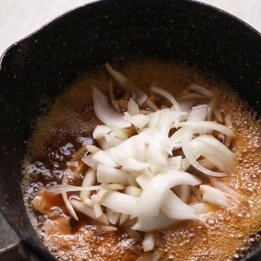 薄切りにした生の玉ねぎを、鶏肉とだし汁が煮立っている鍋に加えている様子