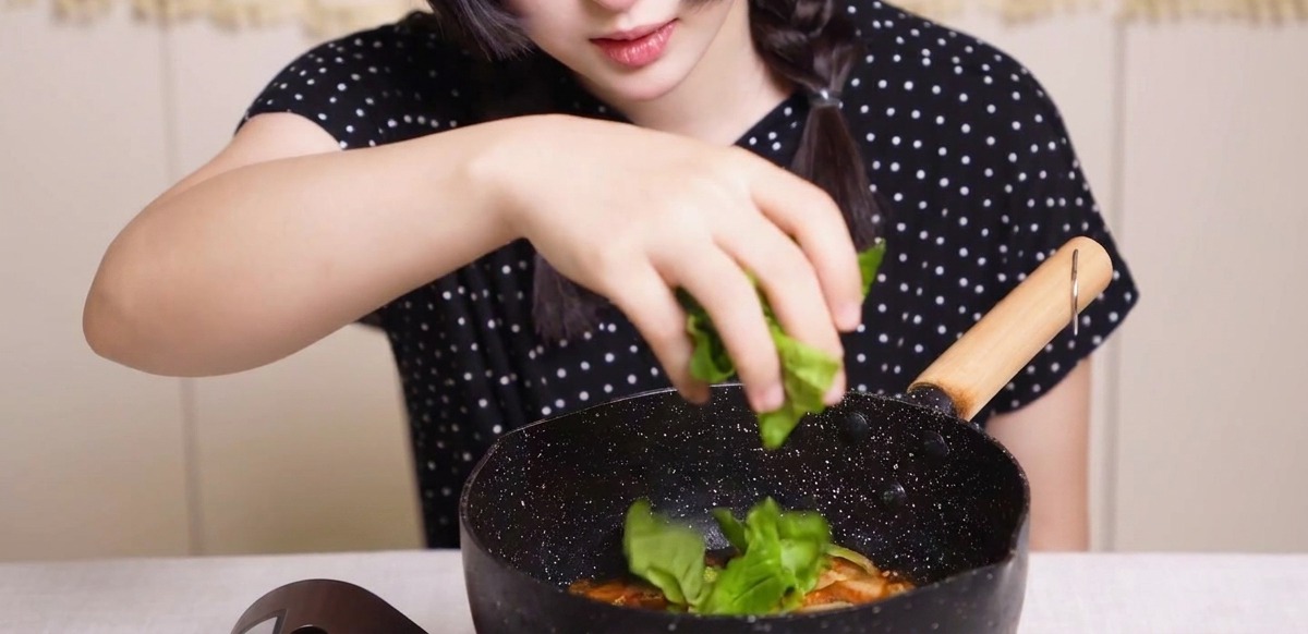 だし汁の中で煮込まれている鶏肉、玉ねぎ、卵の上に、新鮮な青菜を散らしている様子