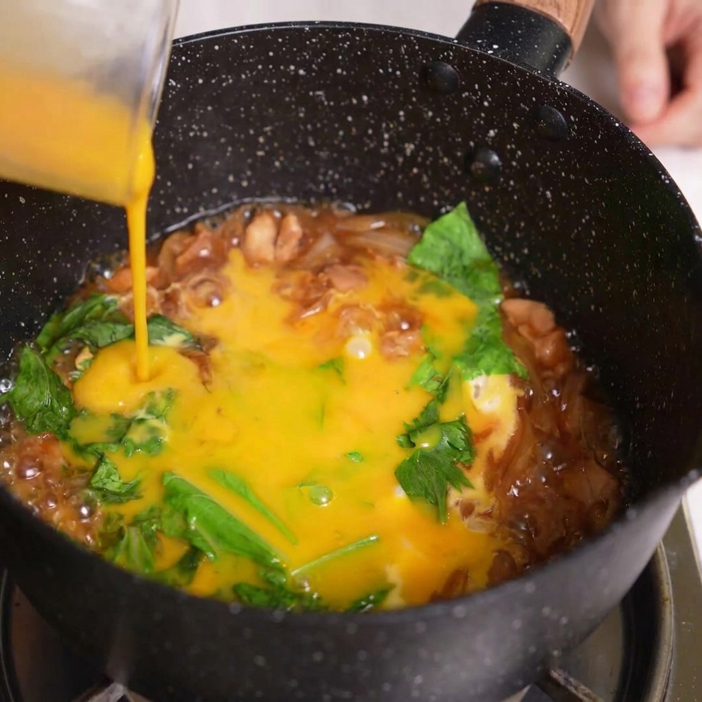 計量カップから残りの溶き卵を、親子丼の具材の上に回し入れている様子