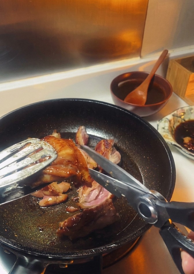 フライパンの中でトングとハサミを使って鶏肉をカットしている様子。
