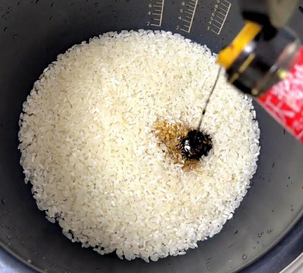 炊飯器の中のお米に、とろみのあるオイスターソースを注いでいる様子。