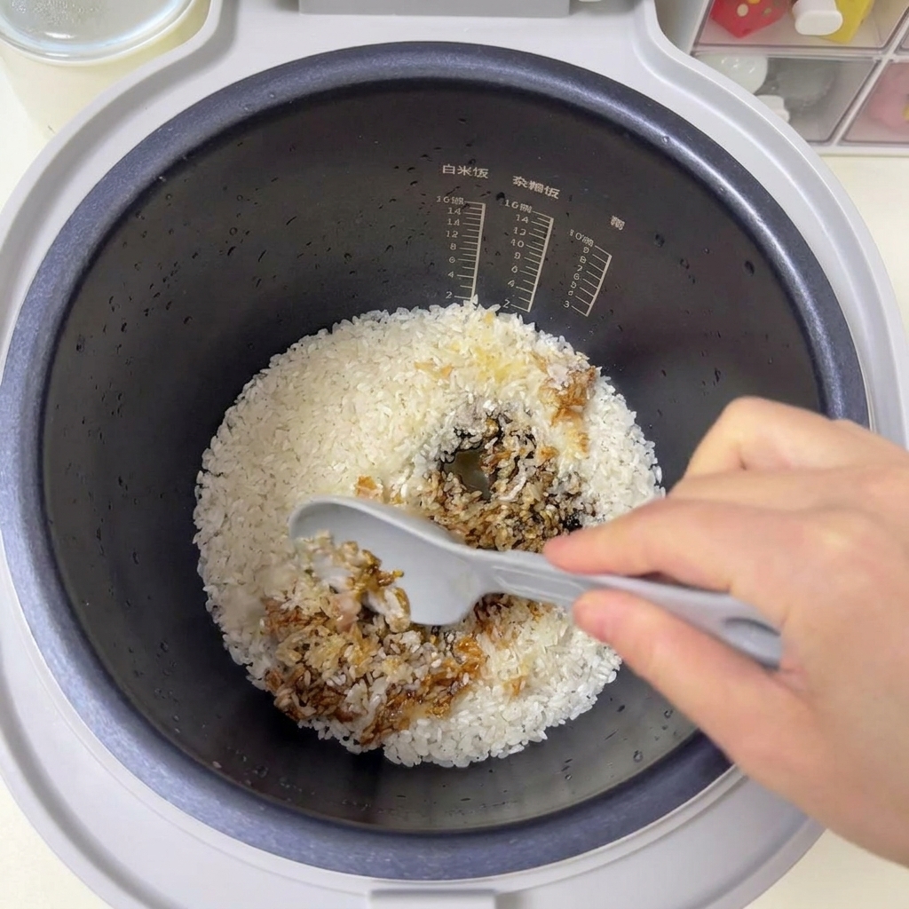 グレーのしゃもじを使って、炊飯器の中のお米とソースを混ぜ合わせている様子。