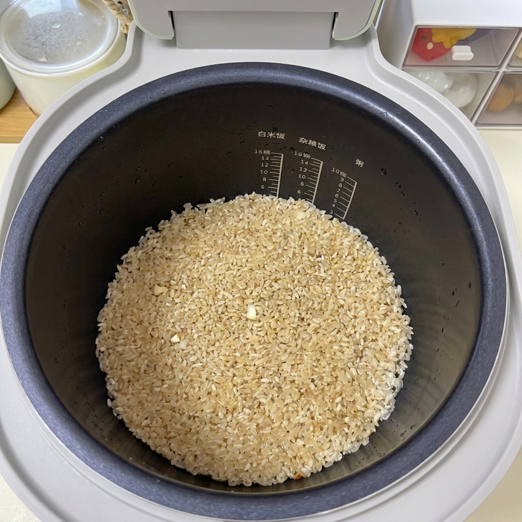 炊飯器の底で、薄茶色に色付いたお米の表面が平らに整えられている様子。