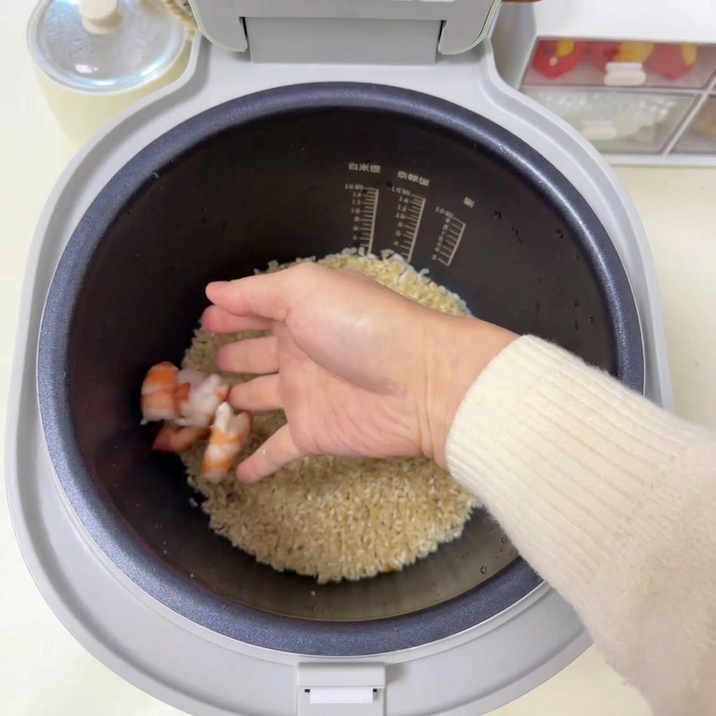 炊飯器のお米の上に、生のピンク色のエビを丁寧に並べている様子。