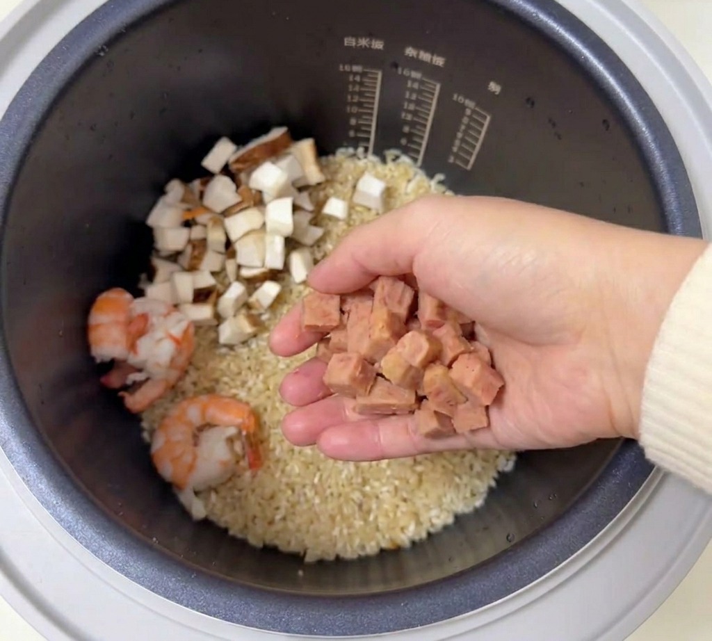 炊飯器の中に、さいの目切りにしたピンク色のランチョンミートを乗せている様子。
