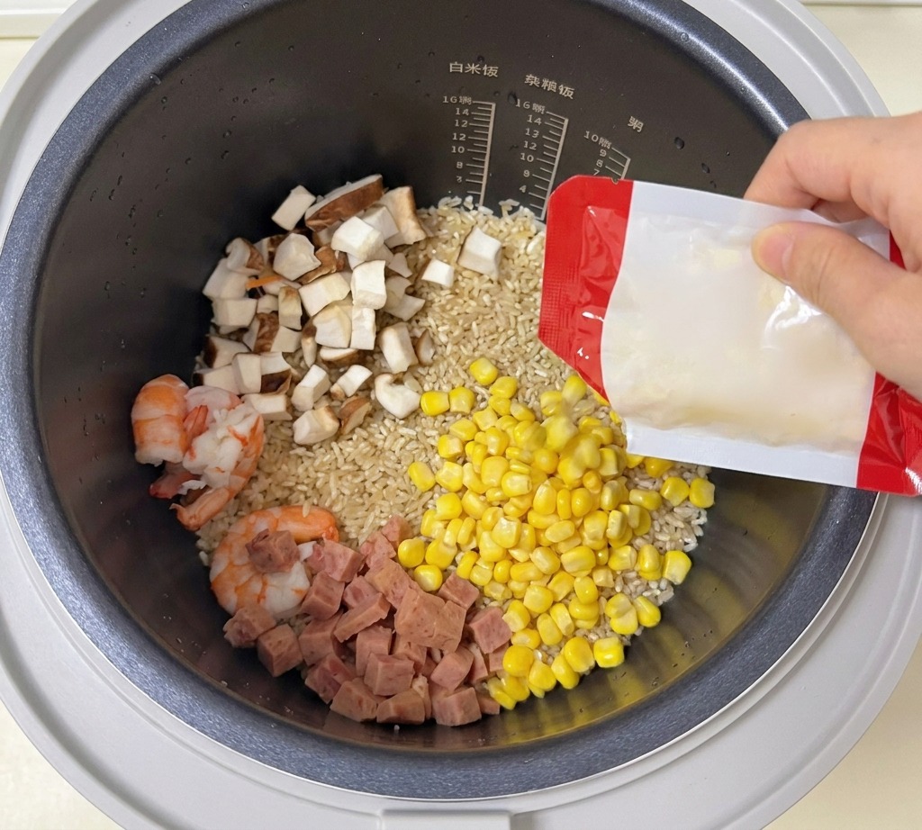 エビや肉が入った炊飯器に、黄色のスイートコーンを振りかけている様子。