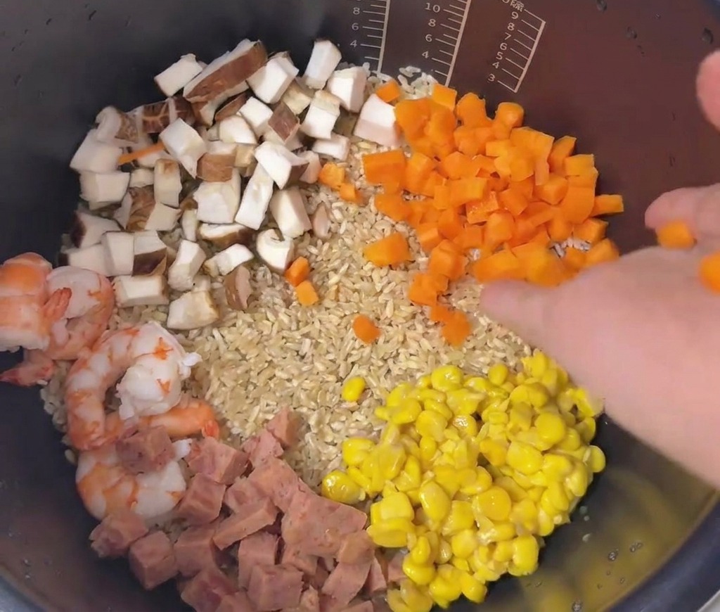 炊飯器の中に、エビ、コーン、肉、椎茸、人参が色鮮やかに並んでいる様子。