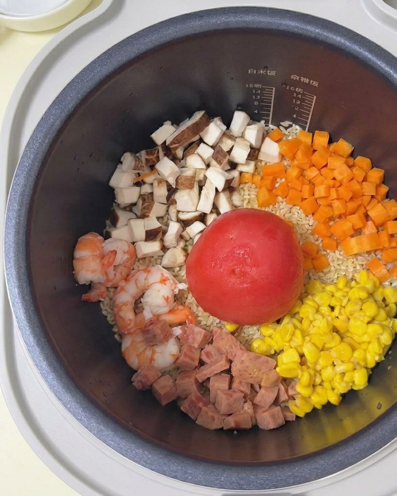 具材が乗った炊飯器に、白いボウルから静かに水を注いでいる様子。