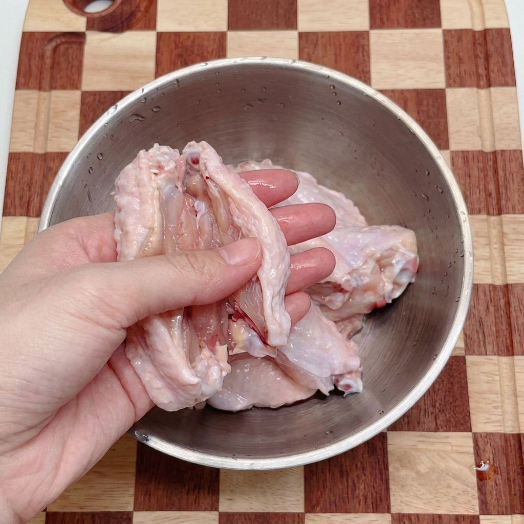 ボウルの中で鶏手羽中をキッチンバサミで半分にカットしている様子。