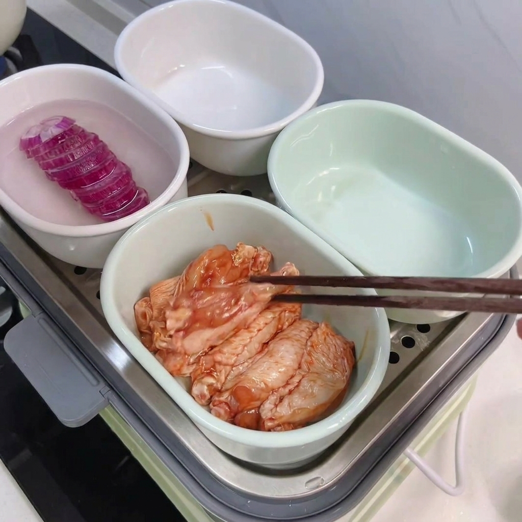 箸を使って味付けした手羽中を別の蒸し用ボウルに並べている様子。
