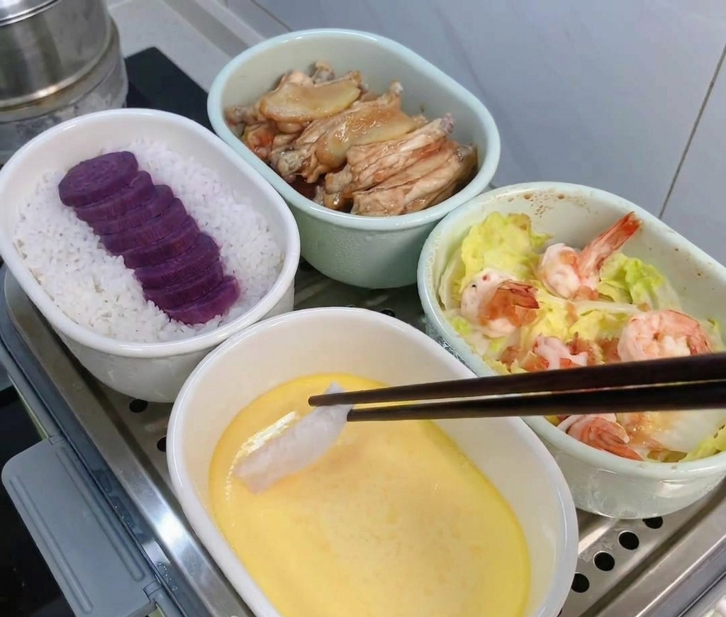 蒸し器の中で少し固まった茶碗蒸しの上に、箸でタラをのせている様子。