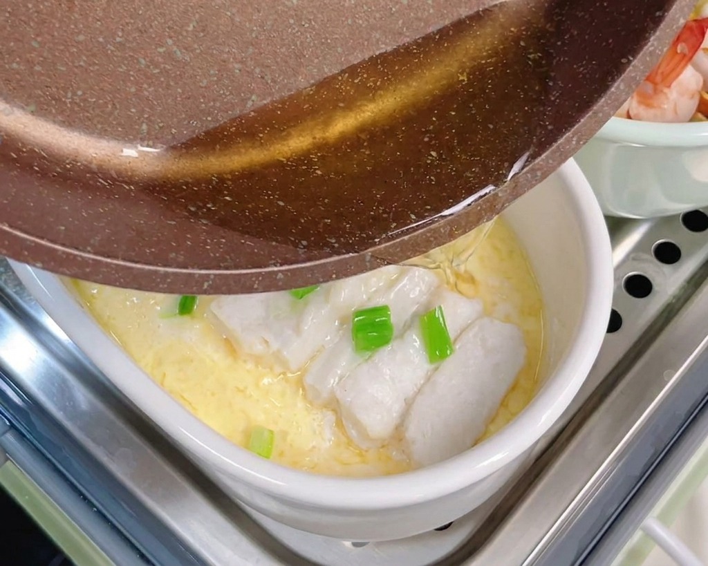 フライパンから熱した油を、ねぎとタラがのった茶碗蒸しにかけている様子。