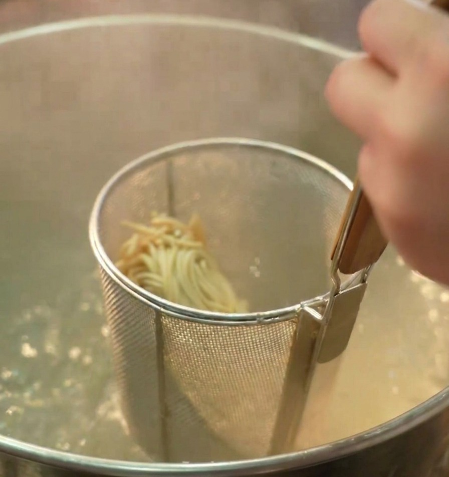 沸騰したお湯の中で中華麺を茹でるテボ