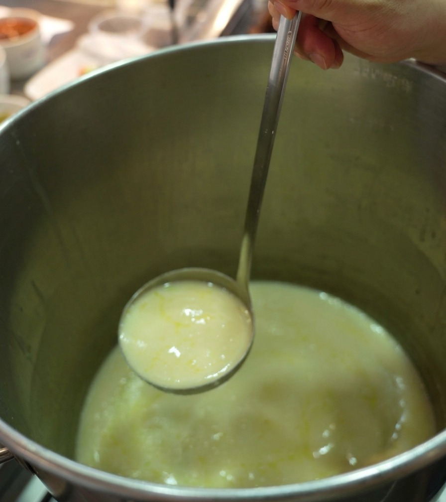 お玉で鶏白湯スープを小鍋に移す様子