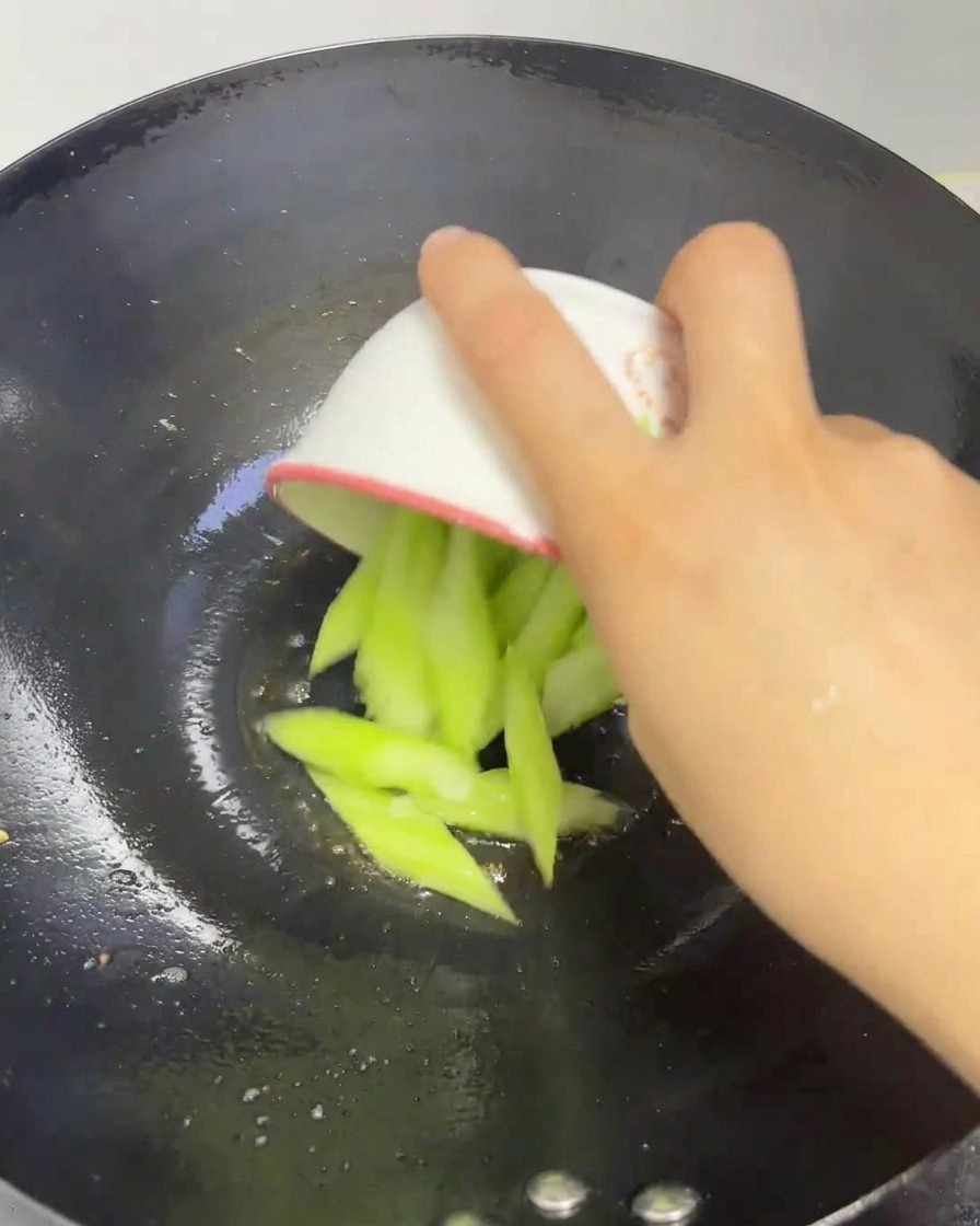ボウルからスライスした新鮮なヘチマを熱した鍋に入れている様子。