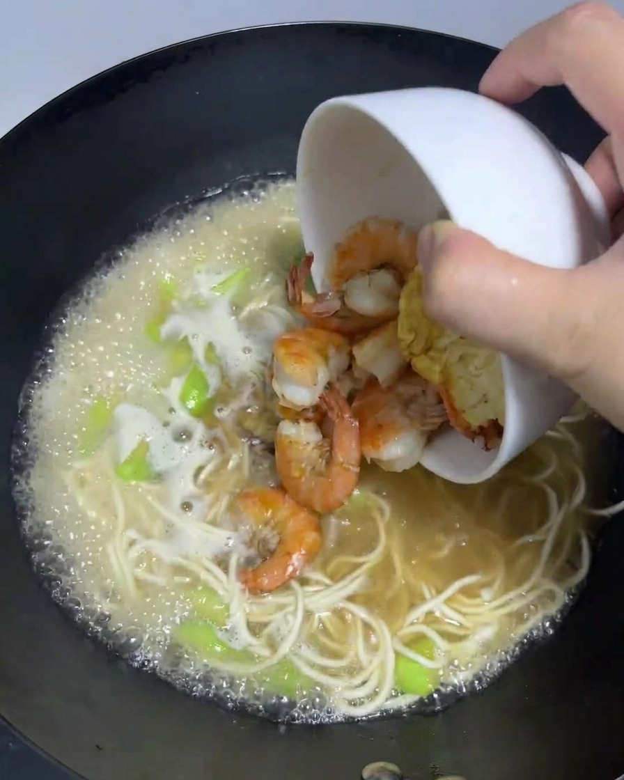 焼いた卵と炒めた海老を、麺が煮えている鍋に戻し入れている様子。