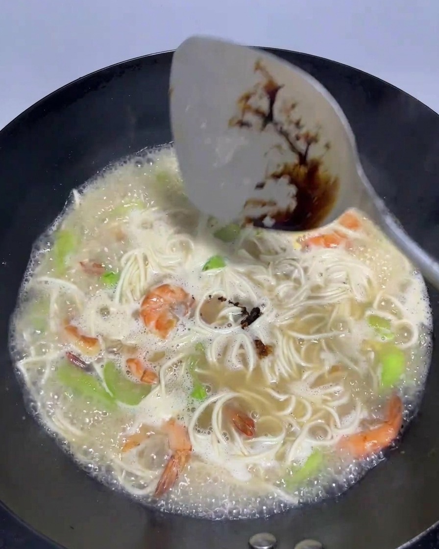 麺や海老が入ったスープに、ヘラで老抽(ダークソイソース)を加えて混ぜている様子。