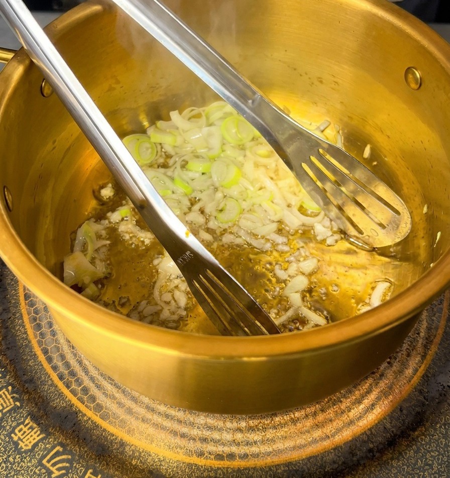 鍋の中で、にんにくとねぎと一緒に豚ひき肉をトングで炒めている様子。