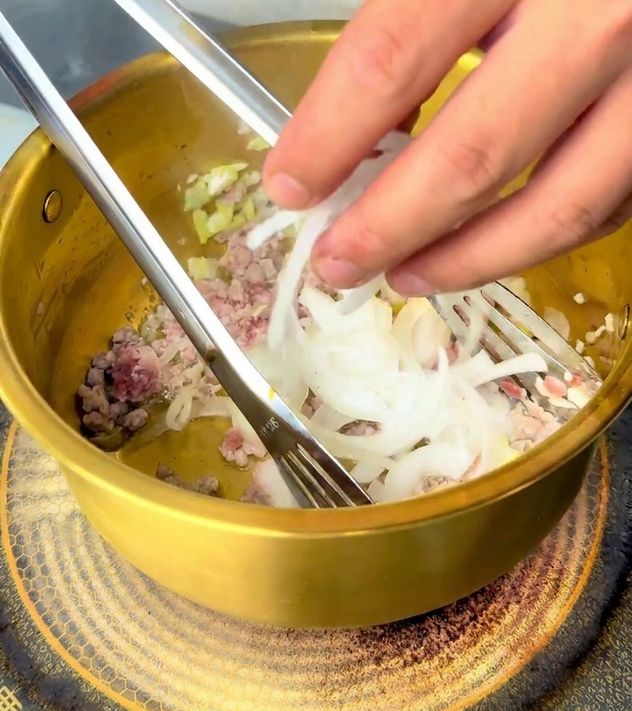 豚肉と香味野菜が入った鍋に、スライスした玉ねぎを加えている様子。