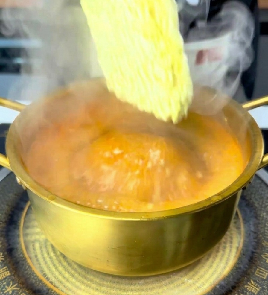 沸騰した赤いスープの中に、インスタントラーメンの乾麺を入れている様子。