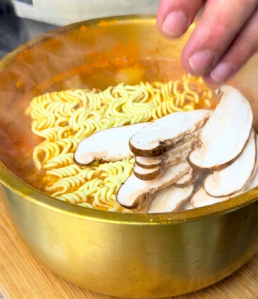 沸騰したスープの中の麺の上に、スライスしたしいたけをのせている様子。