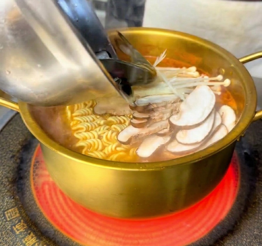 麺とキノコが入った鍋に、新鮮な海老とムール貝を加えている様子。