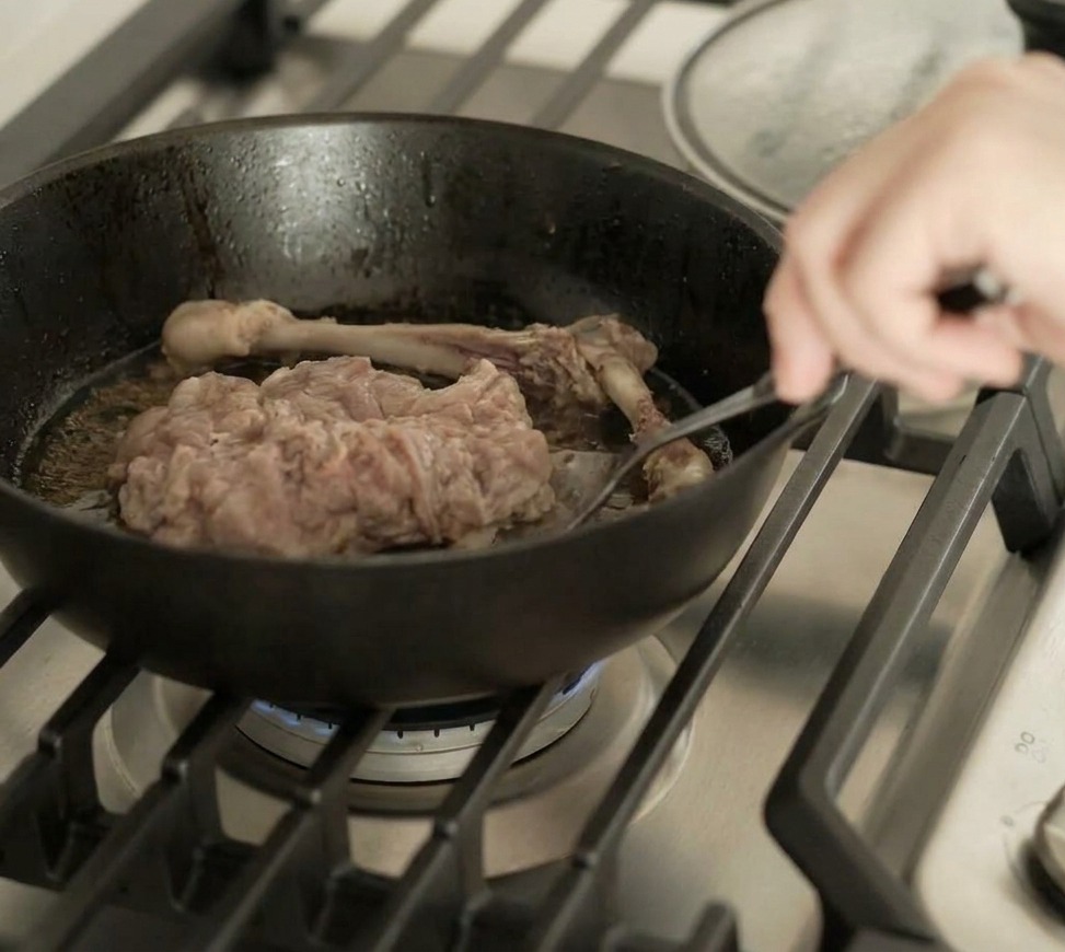 焼き色のついた鴨肉をフライパンの中で裏返す様子。