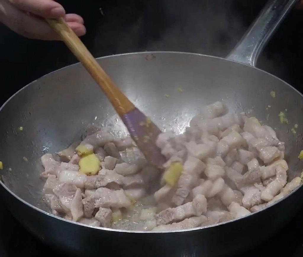 大きなステンレスパンで豚バラ肉とおろし生姜を炒め、脂が出ている様子