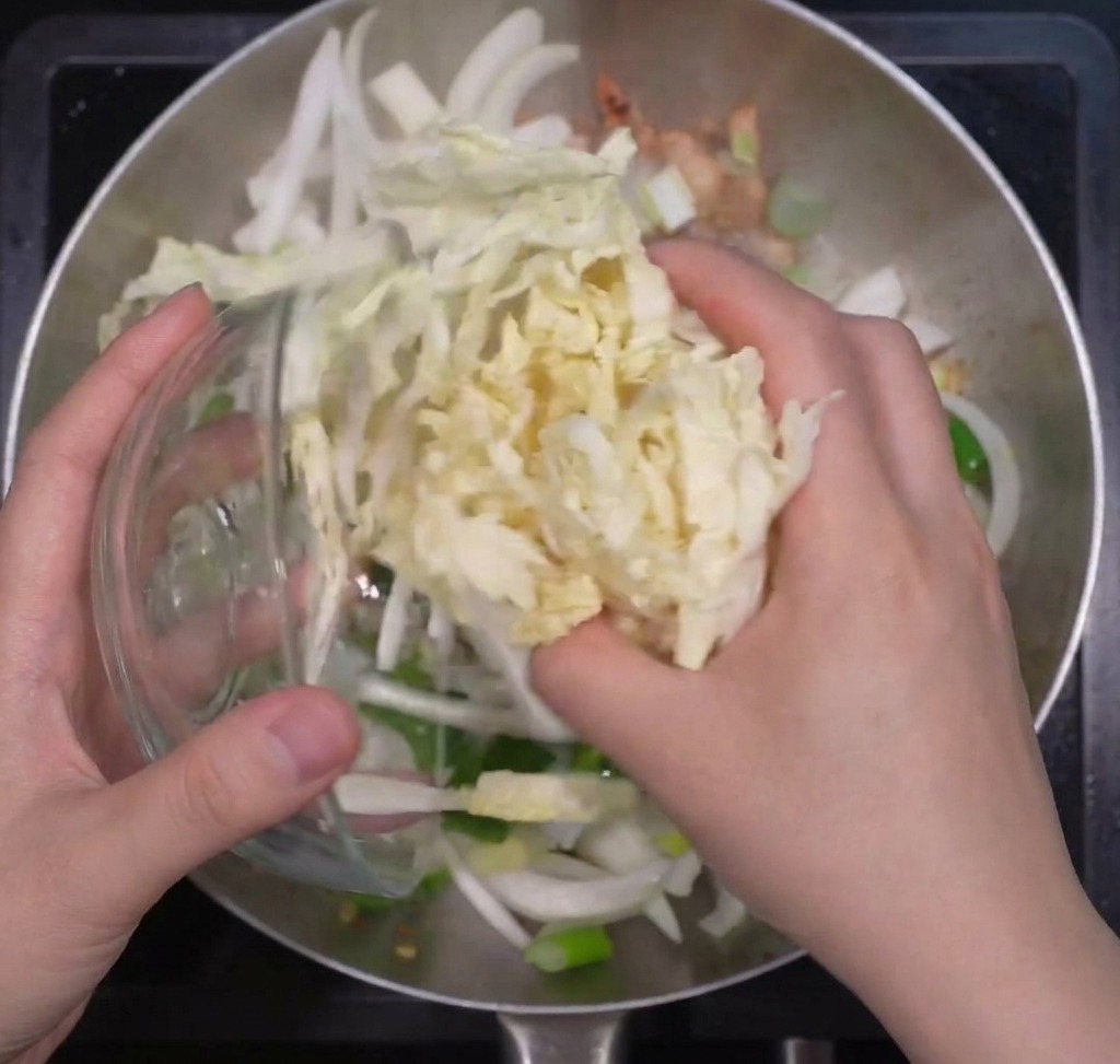炒めた豚肉の上に、たっぷりの白菜、玉ねぎ、チンゲン菜を加えている様子
