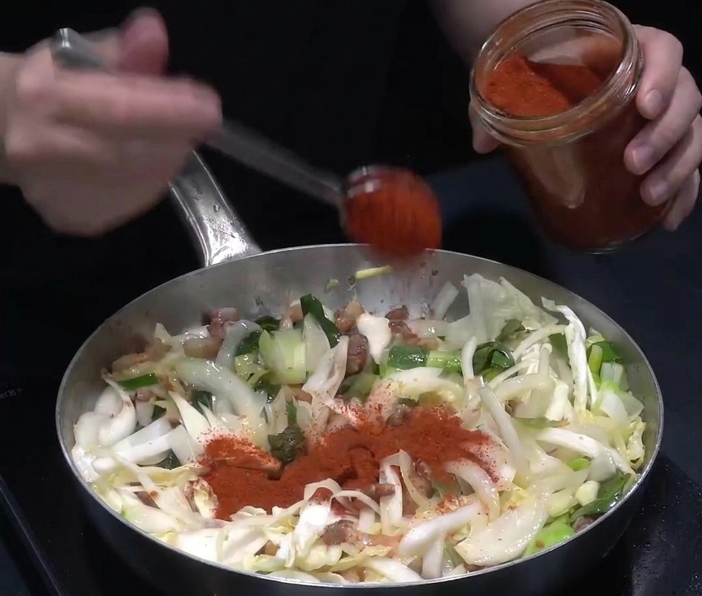 野菜と肉の炒めものに、真っ赤な韓国唐辛子粉をたっぷり加えている様子