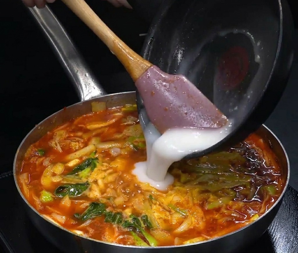 沸騰した赤いスープに、あらかじめ用意した白いルウの液体を注いでいる様子