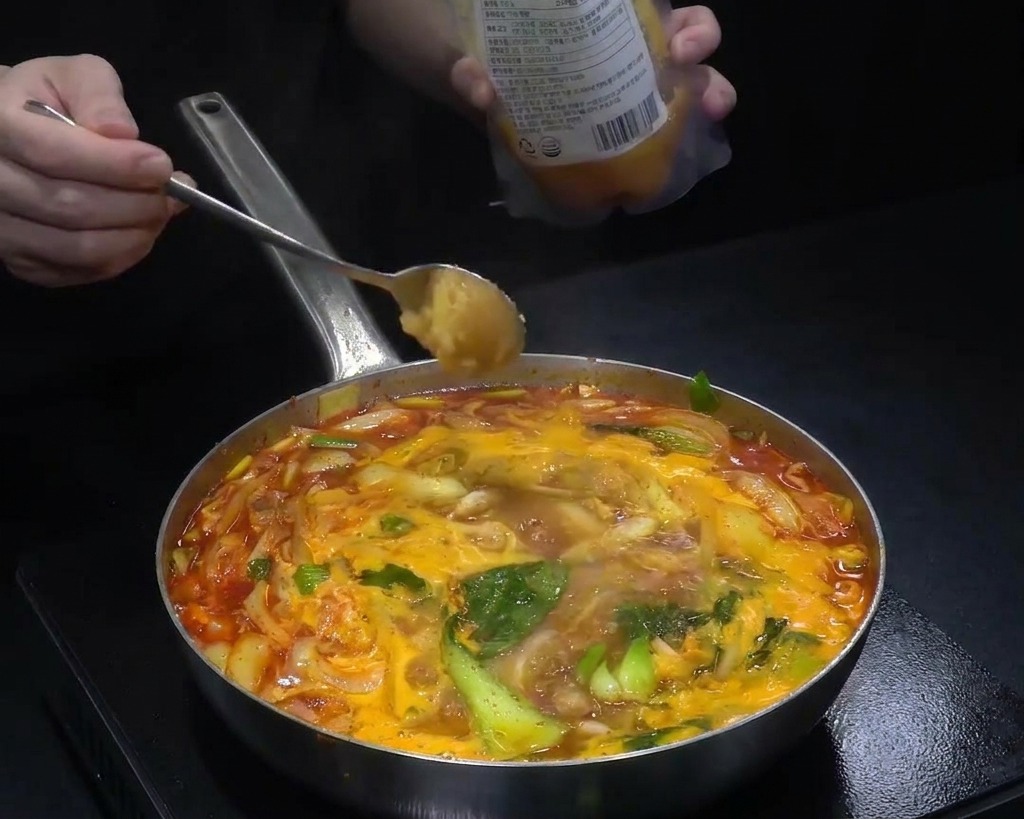 煮え立つ赤いスープに、にんにくや調味料を加えている様子