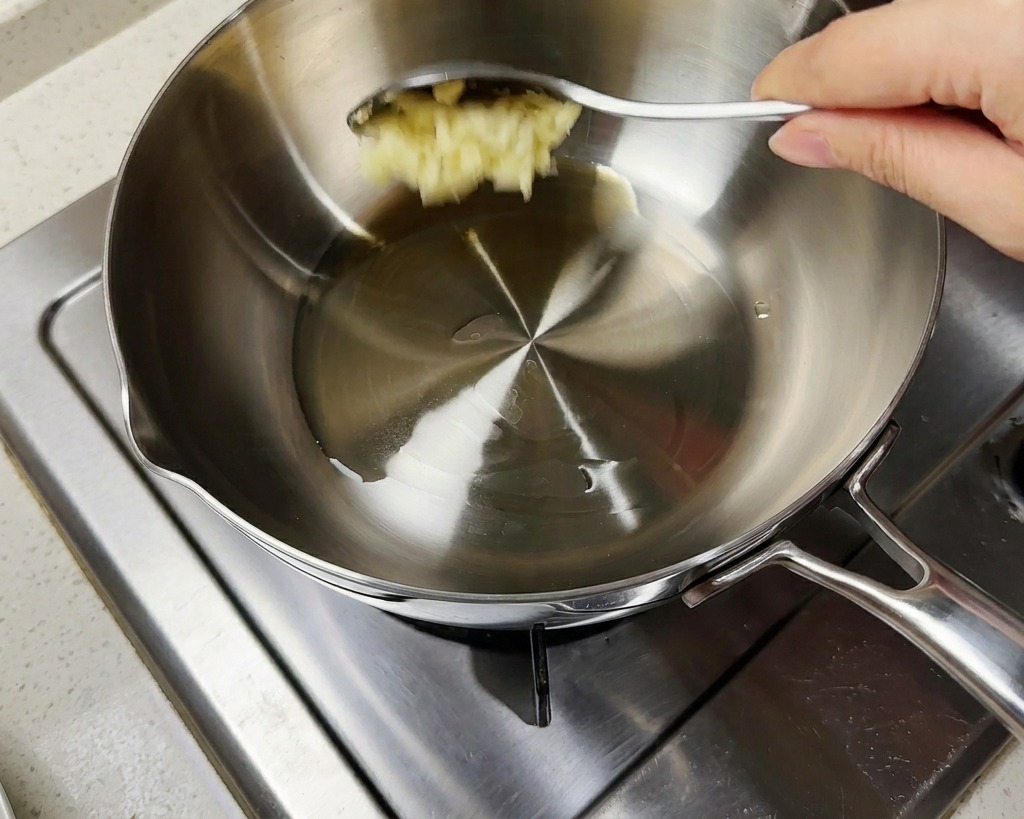 熱した油に、おろしにんにくと刻みねぎをスプーンで加えている様子。