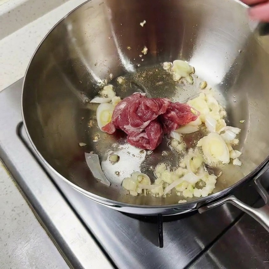 鍋の中で豚肉のスライスが薬味と一緒に炒められている様子。