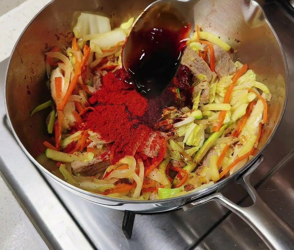 赤く色づいた具材に醤油を回し入れている様子。