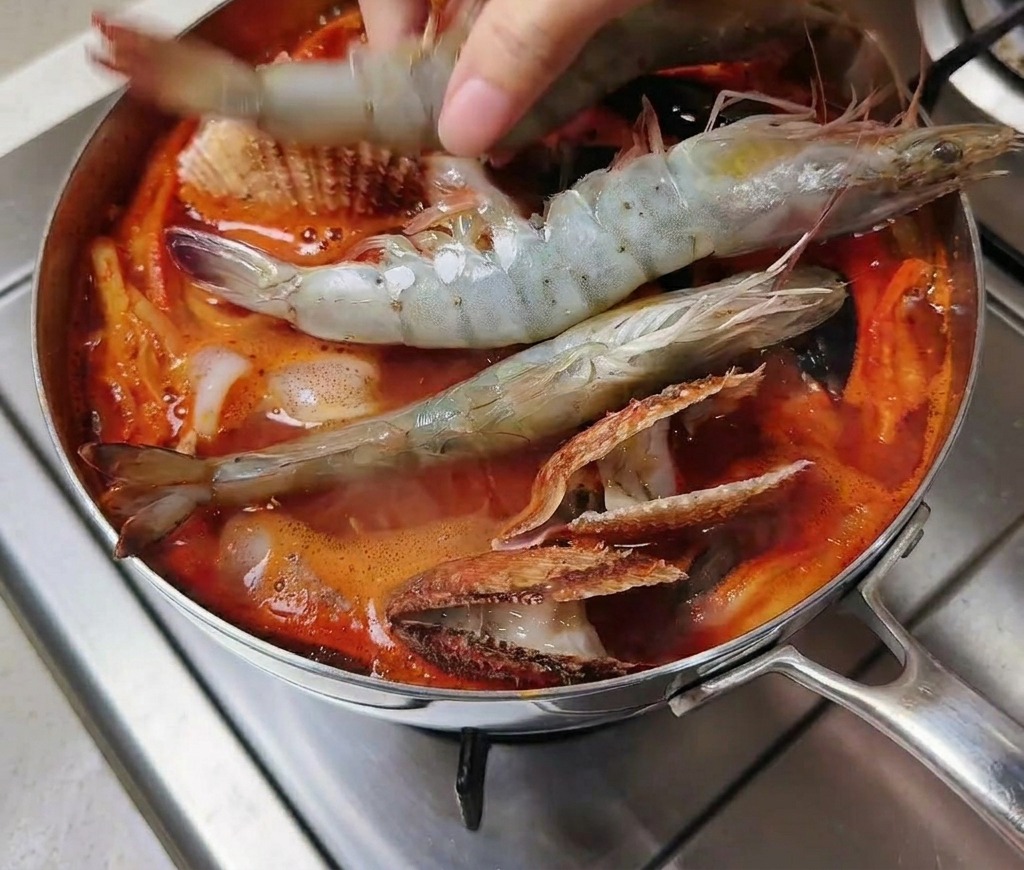 大きなエビを沸騰したスープに一尾ずつ丁寧に入れている様子。
