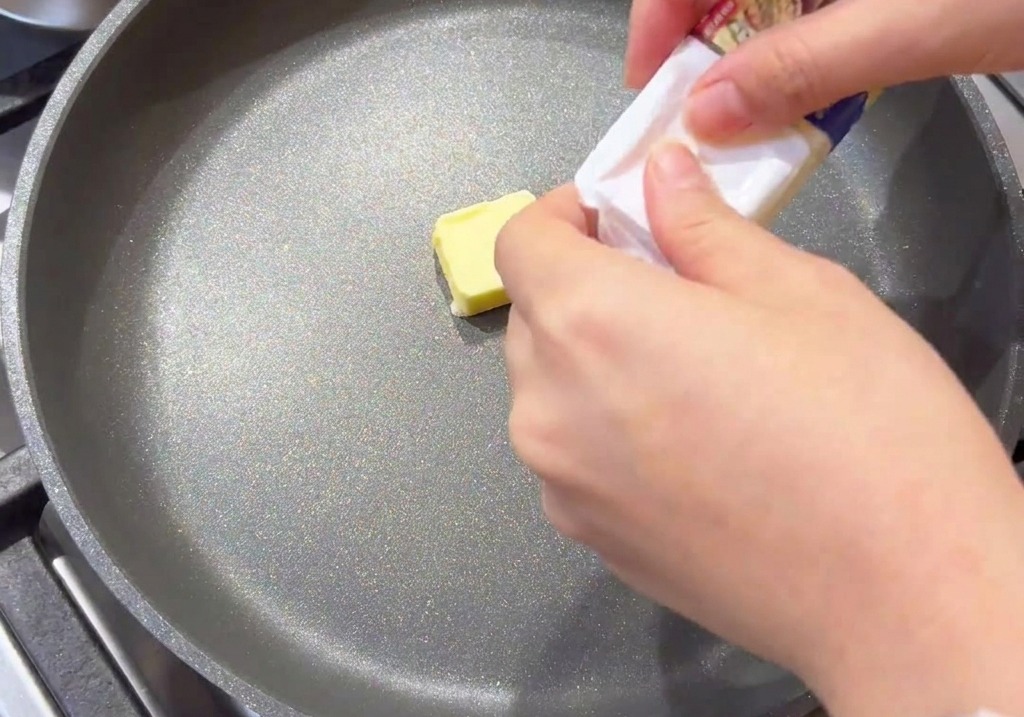 グレーのフライパンの中央で溶け始めている黄色いバターの塊。