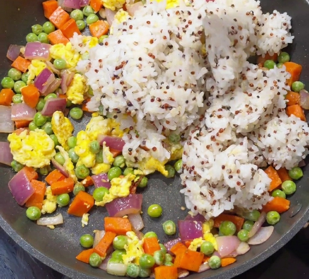 野菜と卵が入ったフライパンに、炊いた白米とキヌアを投入している様子。