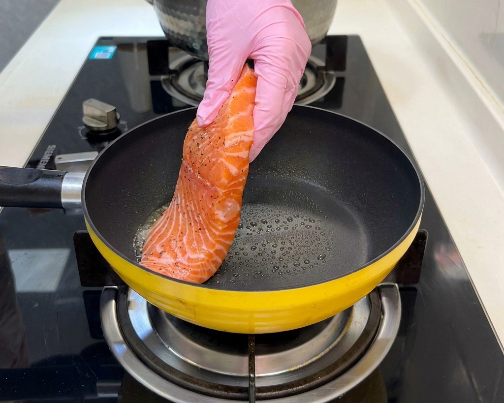 フライパンに下味をつけた生の鮭を並べて焼いている様子。